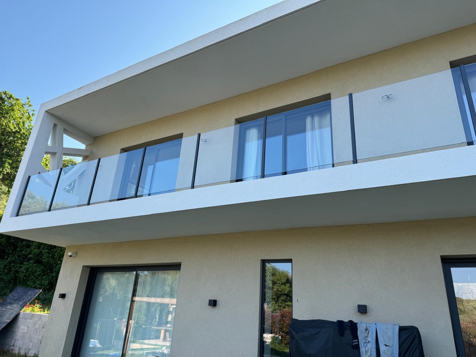Façade contemporaine, enduit clair, auvent béton et garde-corps verre sur balcon-terrasse R+1