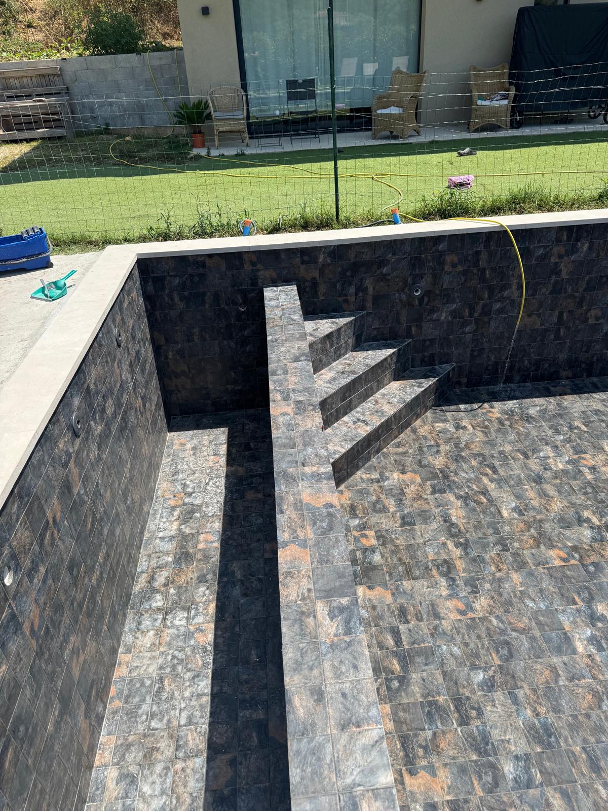 Bassin de piscine terminé en carrelage marbre noir avec escalier d'angle
